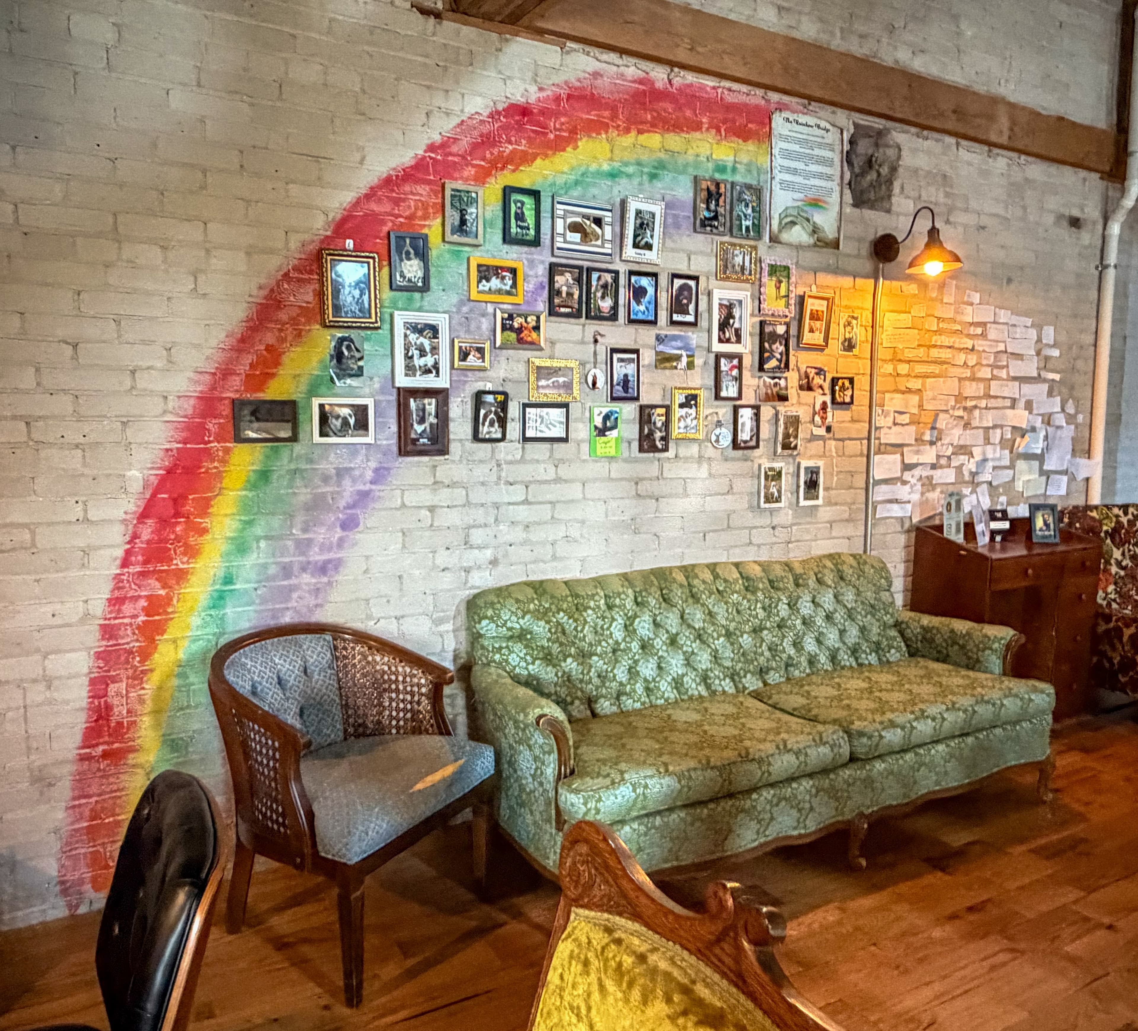 Rainbow mural on a brick wall with framed pet photos above a green tufted sofa.