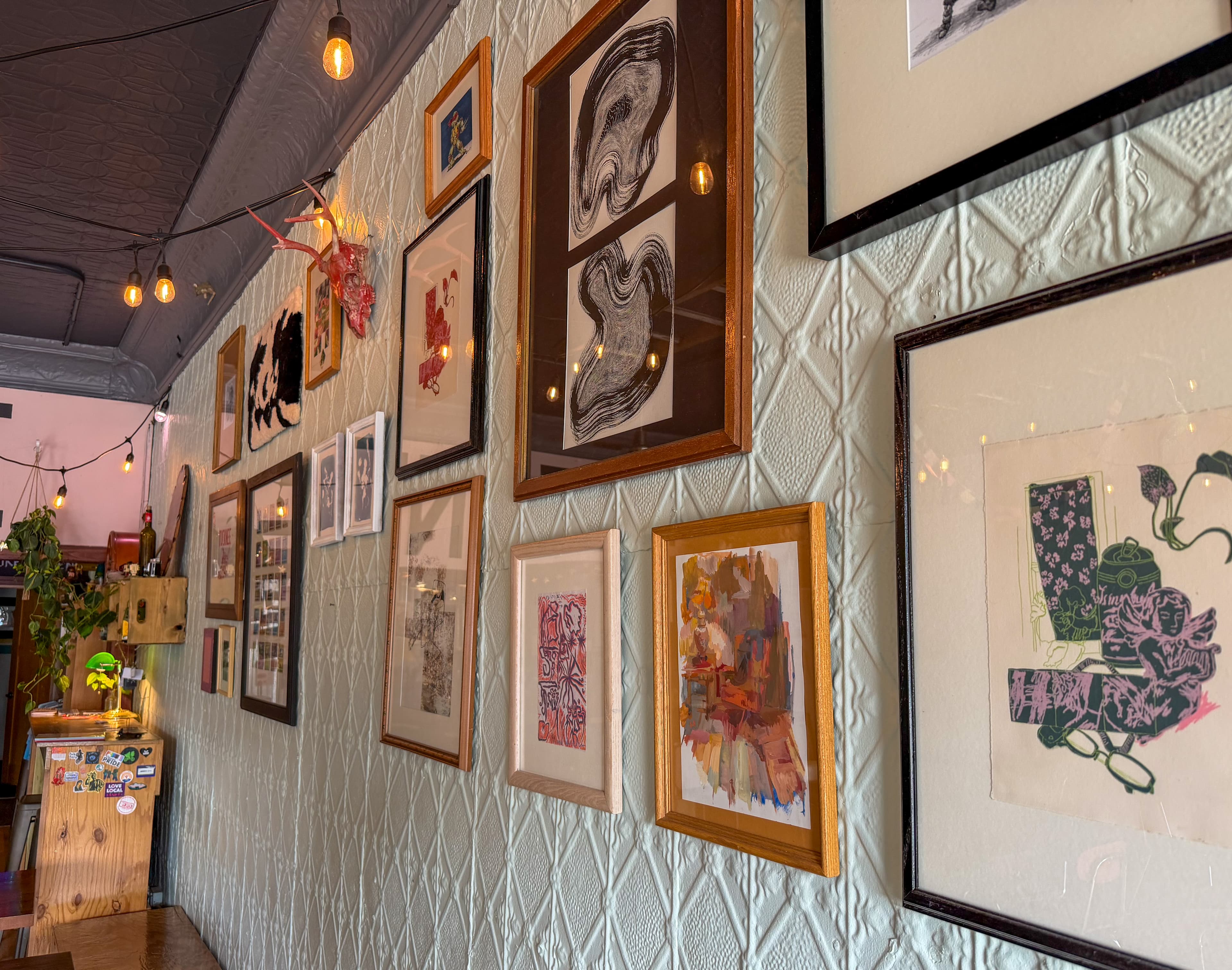 Eclectic gallery wall with framed art and a red deer skull on textured mint wallpaper.